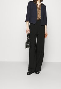 Veste bleu marine à manches trois-quarts portée sur une chemise en satin marron, associée à un pantalon noir taille haute à jambes larges et des chaussures noires.