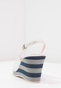 Sandale compensée blanche avec dessus texturé, bride de cheville ajustable et talon compensé rayé bleu et gris.