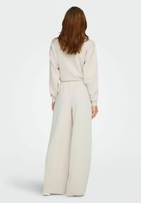 Lysegråt loungewear sæt bestående af en løs pasform top med lange ærmer og brede bukser, lavet af blødt, struktureret stof.
