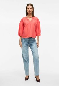 Koralbluse med hjerteformet udskæring og rynkede skuldre, kombineret med lysvaskede, lige ben jeans og mørke hæle. Glat tekstur.