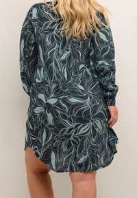 Robe imprimée florale en bleu marine foncé avec des motifs botaniques en teal clair. Elle présente des manches longues et une coupe décontractée avec des fentes latérales.