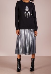 Černá mikina s grafikou rakety, doplněná o plisovanou metalicky stříbrnou sukni a lesklé černé kotníkové boty.