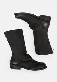 Par de botas negras de cuero hasta media pantorrilla con tacones bajos apilados y cierres de cremallera en la parte posterior, dispuestas planas sobre un fondo claro.