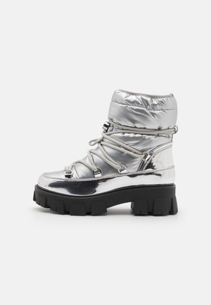 Bottes de cheville argentées réfléchissantes avec un dessus rembourré, des lacets élastiques et une semelle épaisse et chunky noire. Fini brillant avec des accents métalliques.