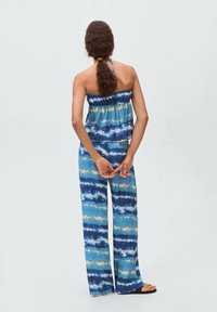 Set format dintr-un top și pantaloni largi cu imprimeu tie-dye în nuanțe de albastru și verde. Material ușor, bandă elastică la top și croială relaxată. Sandalele completează ținuta.