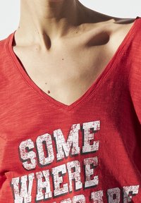 Czerwona koszulka typu v-neck wykonana z miękkiej tkaniny, z białym graficznym napisem "SOMEWHERE", z efektem przetartego druku.