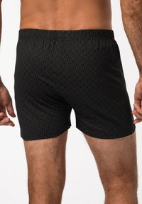 Pantaloni da bagno neri con motivo a diamante, dotati di vita elasticizzata e taglio aderente, che mostrano un tessuto liscio e testurizzato.