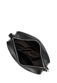 Zwarte leren pouch tas met een zilveren rits. De binnenkant is glad en donker, met een reliëfpatroon van de merknaam. Compacte, minimalistische vormgeving.