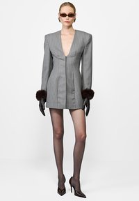 Moteris pasirengusi dėvėti pilką juostelėmis švarką-suknelę su giliu V-kaklu, juodas kailines pirštines su pūkeliu, permatomus pėdkelnius, rudus aukštakulnius ir katės akis primenančius saulės akinius.