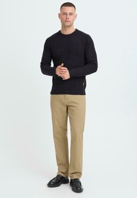 Dunkelgrauer gestrickter Pullover mit langen Ärmeln, kombiniert mit hellbeigen Chinos und schwarzen Schuhen. Auffälliger strukturierter Stoff und taillierte Passform.