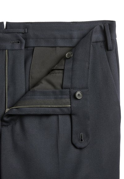 Close-up of dark trousers with open zipper fly, button closure, and visible inner waistband.