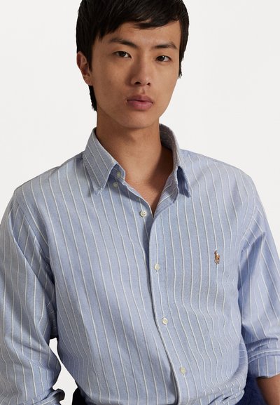 Lichtblauw button-up shirt met witte verticale strepen, voorzien van een klein geborduurd logo op de linkerkant van de borst en een klassiek kraagontwerp.