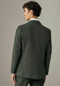 Skræddersyet mørkegrøn uldblazer, to-knaps design, skrå revers, enkelt slids og knapmanchetter. Glat tekstur og struktureret pasform.