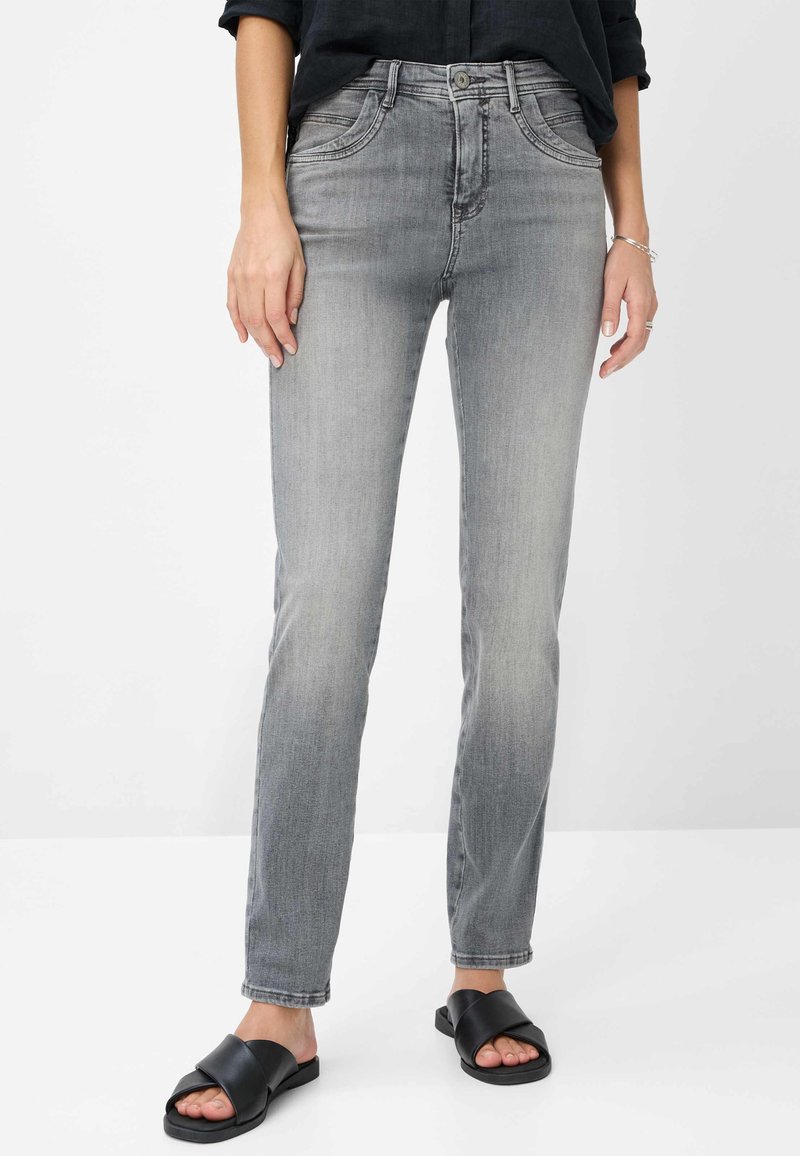 Jean en denim gris avec une coupe slim, comportant des sections décolorées, cinq poches et un zip. Assorti avec des sandales plates noires.