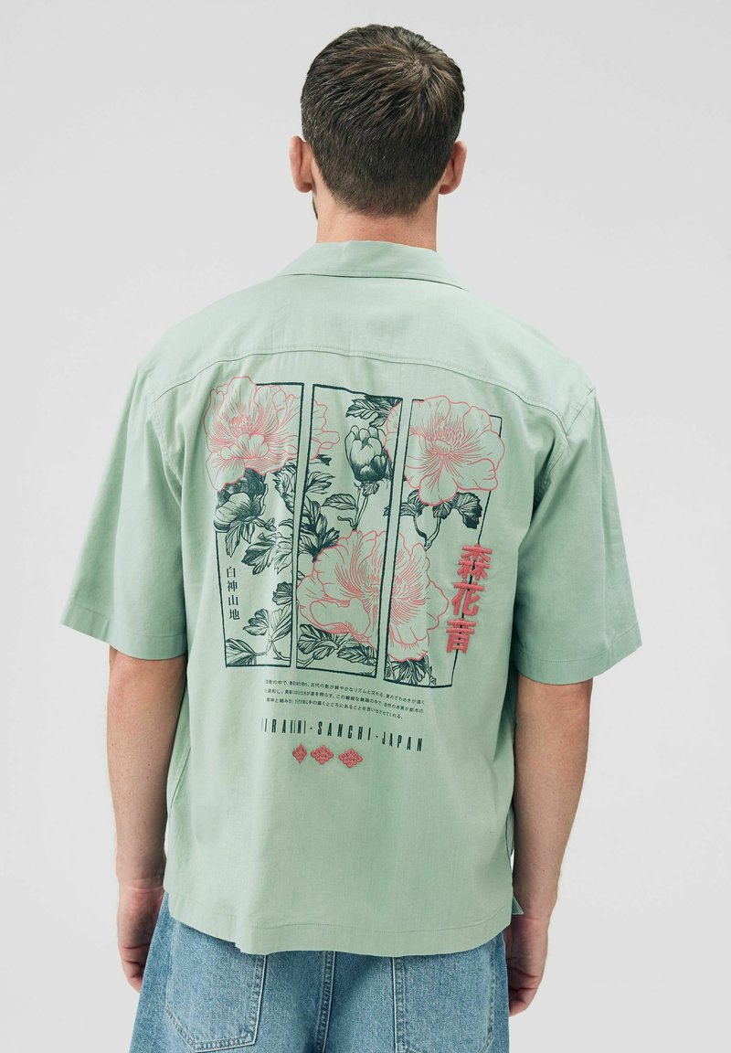 Camicetta a maniche corte in verde menta con motivo floreale sulla schiena, caratterizzata da dettagli in rosa e blu scuro e colletto button-down.