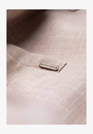 Tissu texturé marron clair avec petite étiquette métallique cousue, gravée du mot « QUINTESSENCE ».