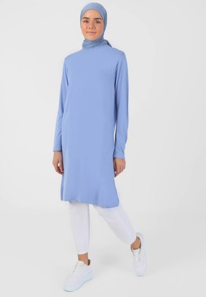 Light blue long tunic with long sleeves, featuring a high neckline, paired with white slim pants and white sneakers. Smooth fabric.