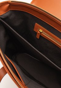 Interieur van een bruinleren tas met een gladde textuur, ritsvak en zwarte stofvoering. Meerdere compartimenten voor georganiseerde opslag.