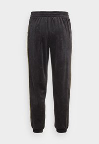 Schwarze Velours-Sweatpants mit elastischem Bund, goldenen Seitenstreifen und gerippten Bündchen. Der Stoff hat ein strukturiertes Muster.
