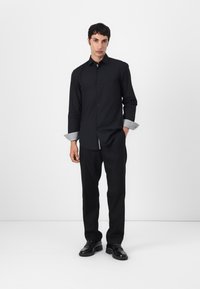 Black button-up shirt with contrasting patterned cuffs, paired with black trousers and shoes. Simple design, tailored fit, smooth texture.