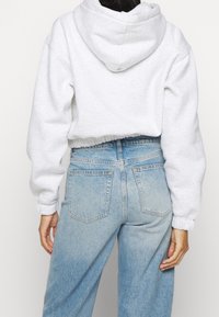 Grey cropped hoodie with a drawstring hood and elastic cuffs, paired with light blue high-waisted jeans featuring back pockets and slight distressing.