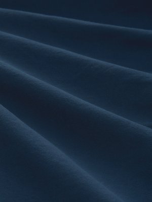 Weiches marineblaues Stoffgewebe mit sanften Falten, die glatte, parallele Rillen bilden und die Textur und Tiefe betonen.