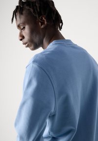 Ανοιχτό μπλε φούτερ με στρογγυλή λαιμόκοψη και ραγλανά μανίκια. Μαλακό ύφασμα με λεία υφή και ελάχιστες ραφές.