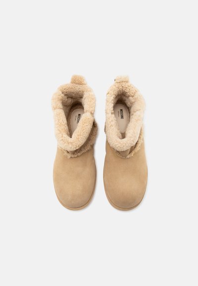 Paire de bottes d'hiver en daim beige avec doublure en shearling moelleux et bouts arrondis, vues de dessus sur fond blanc.