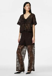 Brown lace two-piece outfit featuring a v-neck top with a tie and wide-leg, semi-sheer pants adorned with floral patterns and sequins.