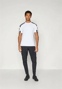Witte sport T-shirt met zwarte accenten op de schouders en mouwen, gecombineerd met zwarte tapered pants en zwarte sneakers. Eenvoudig ontwerp, lichtgewicht stof.