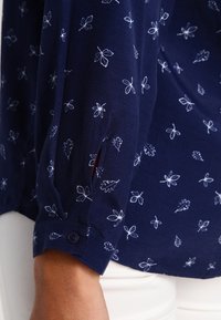 Camicia blu navy con stampa botanica bianca, dotata di maniche lunghe, polsini con bottone e un tessuto morbido e leggero.