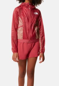 Červená větrovka s předním zipem, kapucí a síťovými bočními panely, spárovaná s odpovídajícími šortkami, obě s logovými akcenty.
