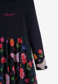 Marineblaues Langarmkleid mit einem strukturierten Oberteil und einem lebhaften, gemusterten Rock, der Blumen, Früchte und Schmetterlinge in leuchtenden Farben zeigt.
