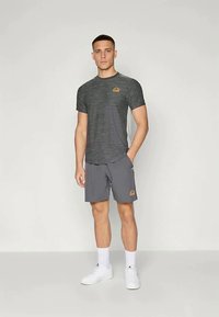 Γκρι αθλητικό μπλουζάκι με διακριτό σχέδιο ρίγας και μικρό λογότυπο στο αριστερό στήθος, συνδυασμένο με γκρι σορτς και λευκές κάλτσες.