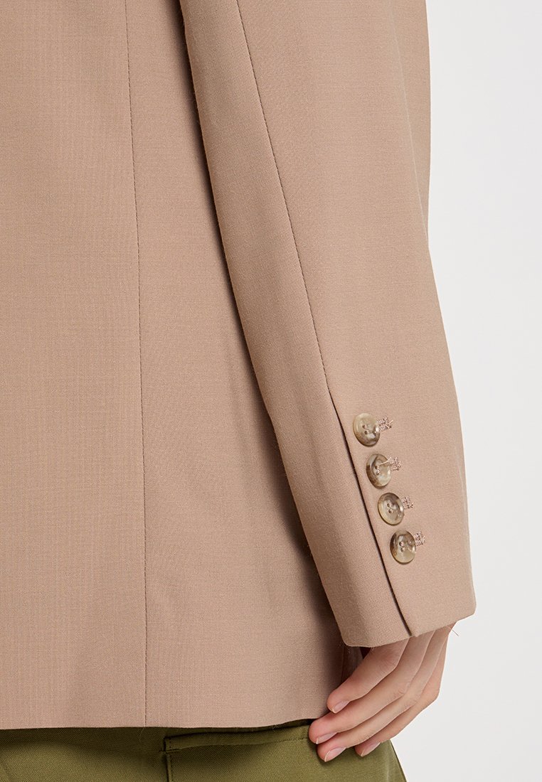 Manica di un blazer beige su misura con quattro bottoni chiari, texture liscia e sottile motivo righe.
