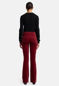 Rode corduroy flared broek met een hoge taille, voorzien van achterzakken en een zachte textuur, gecombineerd met een strakke zwarte lange mouwtop.