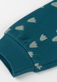 Teal fabric sleeve with light gray tulip-shaped patterns and a cuffed end on a white background.