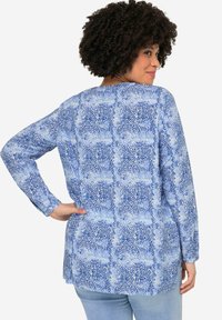 Camisa de manga larga azul con un diseño abstracto, hecha de una tela ligera, con un dobladillo redondeado y un corte holgado.