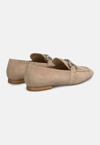 Beige Wildleder-Loafer mit flachem Absatz, die eine dekorative Kettenakzentierung an der Vorderseite aufweisen. Glatte Textur und einfaches Design.