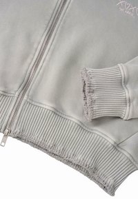 Grijze zip-up sweatshirt met geribbelde zoom en manchetten, met een zachte textuur en een lichtroze geborduurd ontwerp.