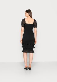 Vestido preto ajustado com mangas bufantes, corpete franzido e bainha em camadas com babados. Feito de um tecido leve com detalhes transparentes e textura.