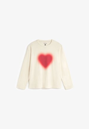 Long-sleeve cream cotton t-shirt featuring a red spray-painted heart design at the center. Crew neck with a relaxed fit and stitched hem.