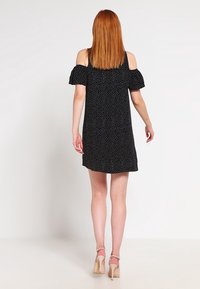 Musta pallohaalarein mekko, jossa on kylmät olkapäät, lyhyet hihat ja rento malli. Sujuva kangas ja polvien ylle ulottuva pituus.