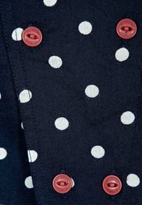 Tessuto blu navy con pois bianchi e due bottoni rossi. La texture appare tessuta, con una finitura liscia e motivi coerenti.