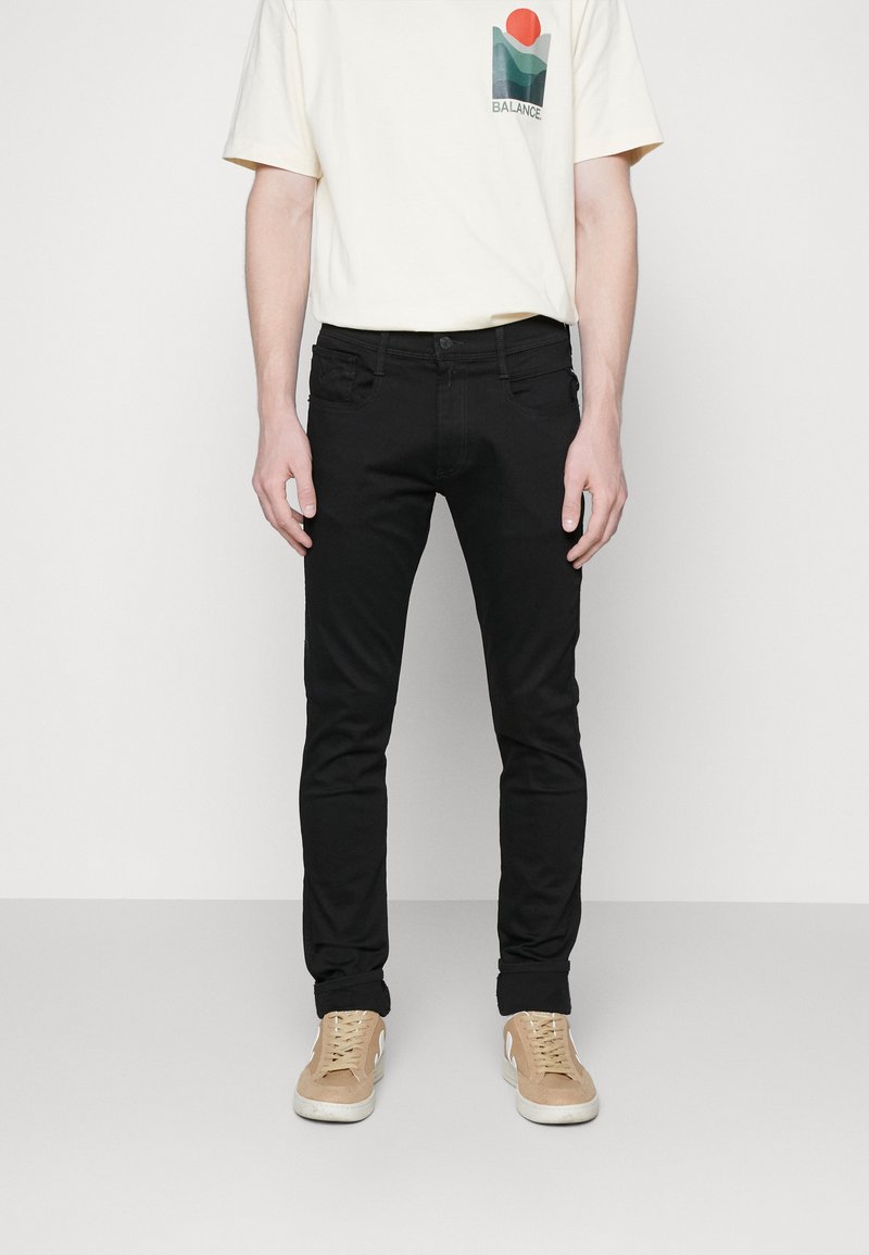 Schwarze Slim-Fit-Jeans aus Denim, mit Vorder- und Hintertaschen, genähten Nähten und einem klassischen Knopfverschluss. Kombiniert mit einem cremefarbenen T-Shirt.