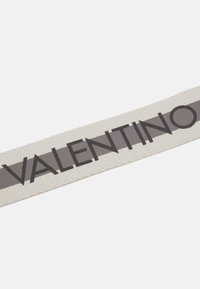 Valentino logo patch, cream fabric with a textured finish, featuring bold black lettering on a contrasting gray background.