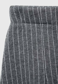 Grauer Stoff mit vertikalen weißen Streifen, der eine glatte Textur und ein breites Taillenband-Design aufweist. Nahansicht, die die Steppdetails zeigt.