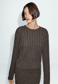 Maglione marrone a filo intrecciato con scollo rotondo e polsini a coste. Tessuto testurizzato con una vestibilità morbida, abbinato a un capo inferiore coordinato.