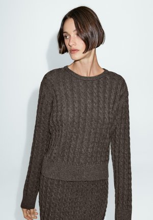 Brown cable-knit sweater with a round neckline and ribbed cuffs. Textured fabric with a loose fit, paired with matching bottom garment.