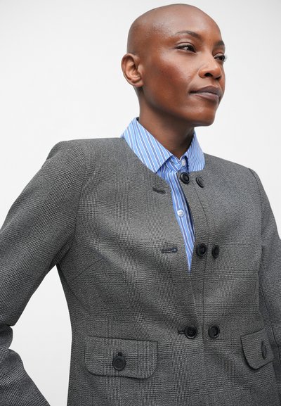 Grijze geruite blazer met een gestructureerde pasvorm, twee zwarte knopen en voorzakken. Daaronder een blauw gestreept overhemd met een kraag.
